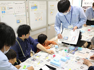 先生が紙を持って作り方を教えている様子