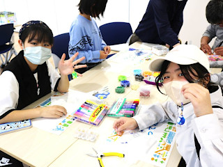 女の子2人が作成したストラップをカメラに向けている様子