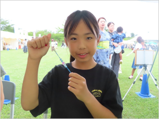 完成した青とピンクのアクセサリーを嬉しそうに掲げて見せる女の子の写真