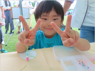 アクセサリーを持ちながら、両手でピースサインをして微笑む男の子の写真