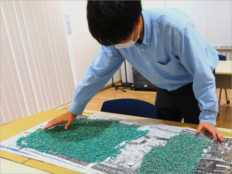 新聞紙の上に緑色の材料を広げて準備するスタッフ