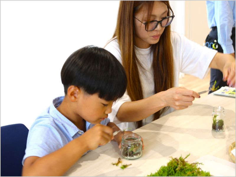 ガラス瓶の中に苔を配置し、飾り付けている親子の様子