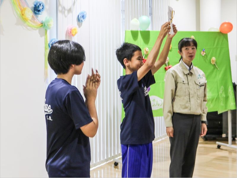 スタッフと記念品を掲げる生徒代表の少年